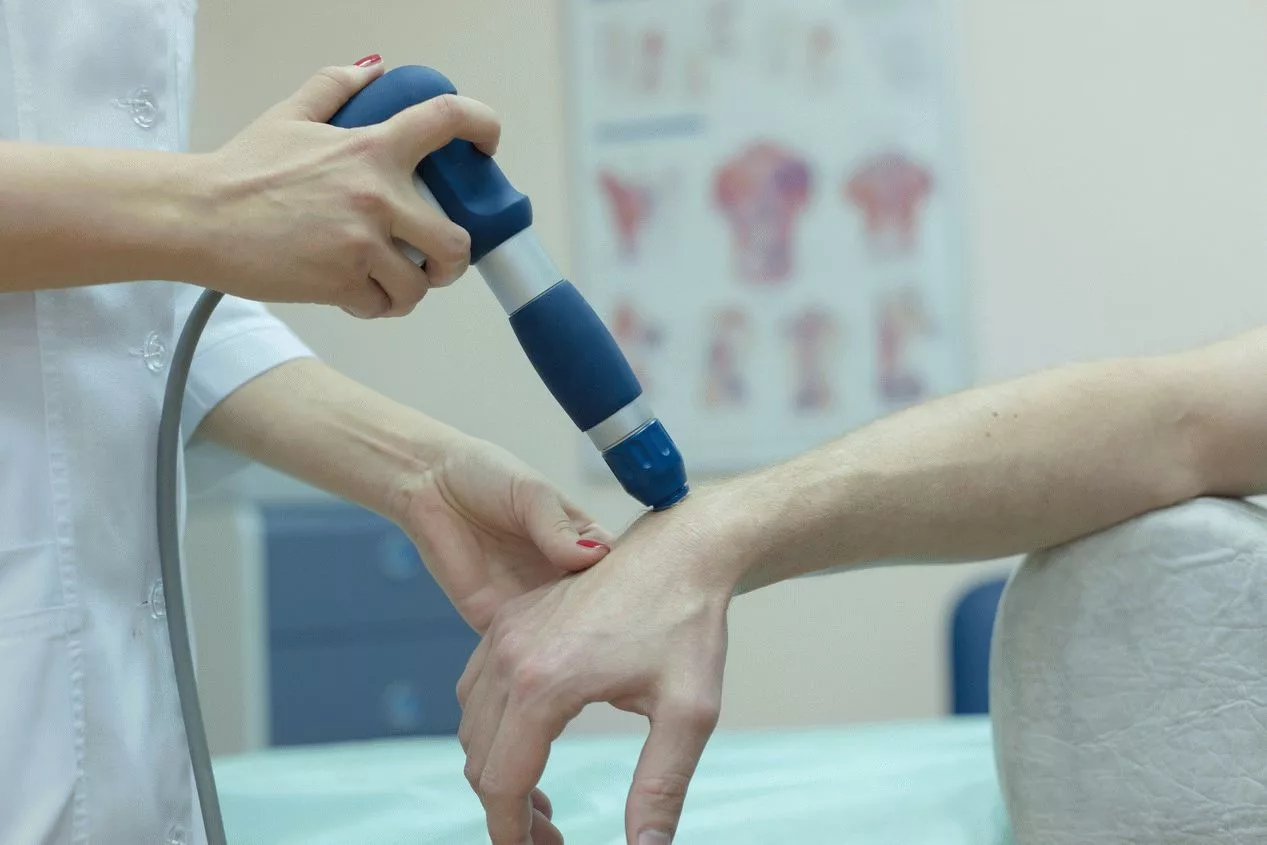 A patient receives shockwave therapy on their wrist in a medical clinic.